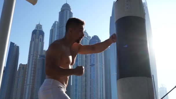 Kaslı Adam arka planda Dubai şehir manzarasıyla kum torbasına vuruyor. — Stok video
