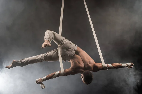 Sirk sanatçısı hava kayışları ile güçlü üzerinde duman arka plan üzerinde kasları
