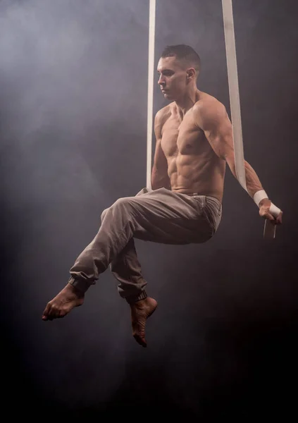 Circus artist op de luchtfoto bandjes met sterke spieren op de achtergrond van rook — Stockfoto