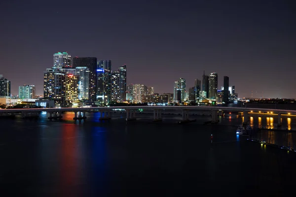 Vista panorámica del horizonte de Miami al atardecer con rascacielos urbanos y puente sobre el mar con reflejo — Foto de Stock