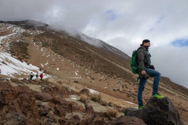 Sırt çantalı, dağın tepesinde dijital kamerası olan genç bir adam. Seyahat ve blog yazma kavramı
