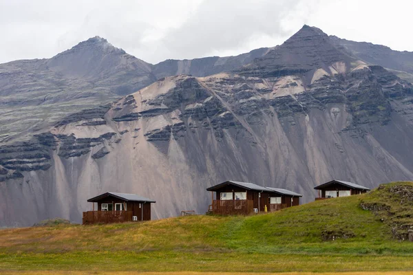 Small houses on hill in Iceland with and green field and mountain peak on background