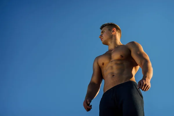 Hombre musculoso guapo posando con fondo de cielo azul. Concepto de estilo de vida saludable —  Fotos de Stock