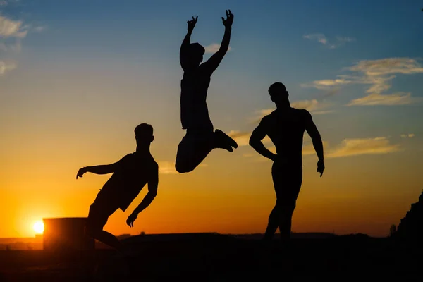 Groupe de jeunes gens heureux sautant sur le toit avec coucher de soleil sur le fond — Photo
