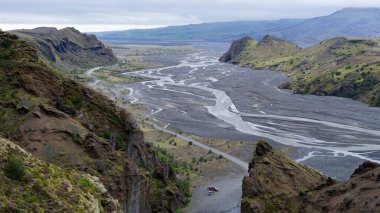 Bir grup turistin bulunduğu kırmızı araba, geniş bir ırmağın olduğu kanyona park edilmiş. İzlanda 