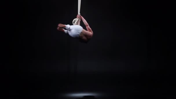 Muskulöser Zirkusflieger an den Antennenbändern im schwarzen Studio — Stockvideo