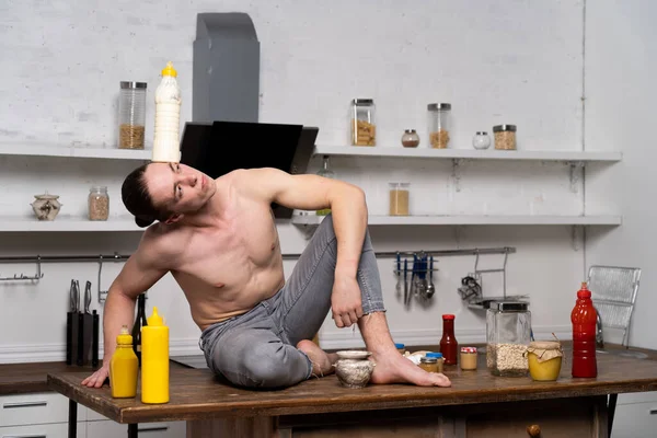 厨房里一个肌肉发达的男人和苏打水坐在一起的照片 — 图库照片