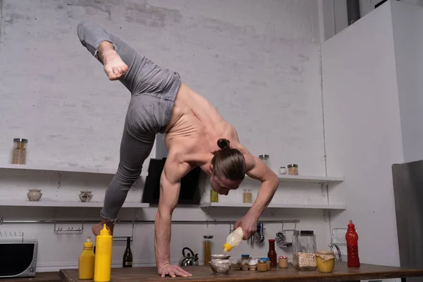 Musclé homme debout sur une main dans la cuisine et tenant bouteille avec de la sauce. Concept de mode de vie sain et d'alimentation biologique — Photo