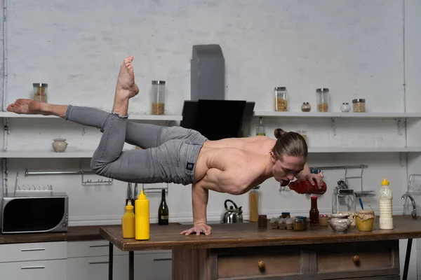 Musclé homme debout sur une main dans la cuisine et bouteille d'équilibre avec souse. concept de cuisine créative . — Photo