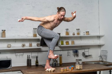 Mutfakta yumurtaları dengeleyen kaslı bir adamın yaratıcı fotoğrafı. 