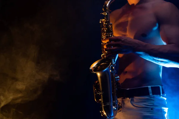 Gespierde man met naakte romp spelen op saxofoon met gerookte kleurrijke achtergrond — Stockfoto