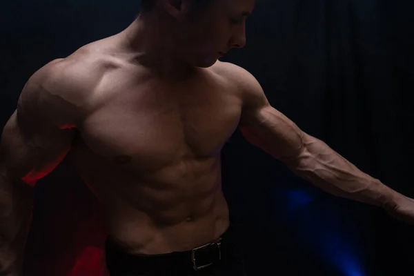 М'язистий чоловік показує м'язи ізольовані на чорному тлі з кольоровим димом. Концепція здорового способу життя — стокове фото