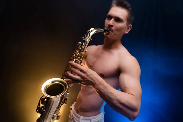 Uomo muscoloso con busto nudo che suona su sassofono con sfondo colorato affumicato — Foto Stock