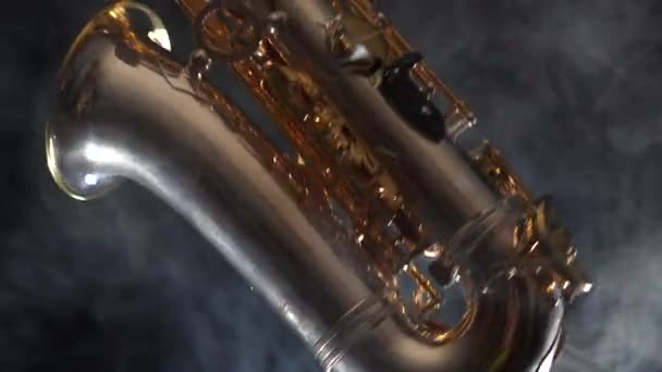 Gouden glanzende altsaxofoon langzaam bewegen op zwarte achtergrond met rook — Stockvideo