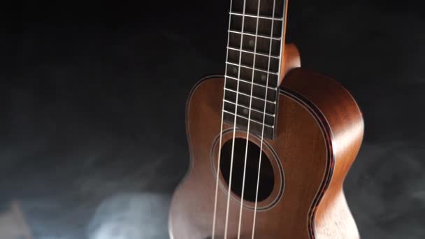 Guitarra ukelele Hawai de madera roja aislada sobre fondo negro con humo — Vídeo de stock