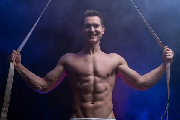 Musculoso artista de circo masculino con correas aéreas sobre fondo negro y ahumado —  Fotos de Stock