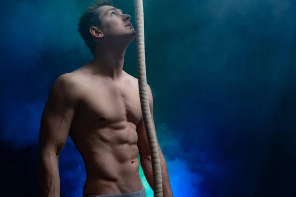 연기에 그을린 배경 위에 줄을 드리우는 근육질의 남자 서커스 가수 — 스톡 사진