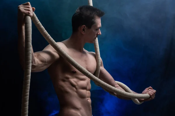 Muscular male circus artist with Cord Lisse on black an smoked background — Stock Photo, Image