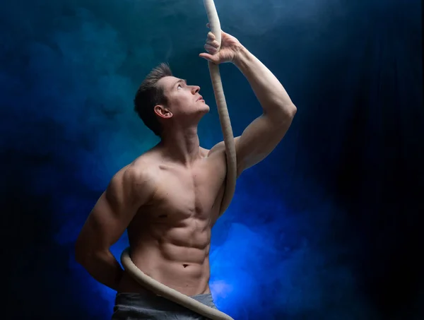 Muscular male circus artist with Cord Lisse on black an smoked background — Stock Photo, Image