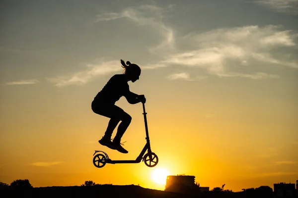 Silhuet af en mand ridning og hoppe på kick scooter med smuk solopgang på baggrund - Stock-foto