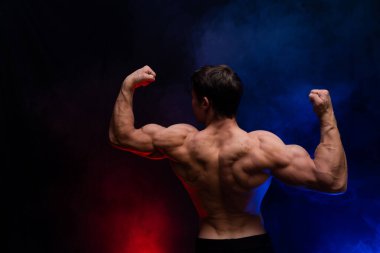 Siyah arka planda renkli dumanla izole edilmiş kasları gösteren kaslı bir adam. Sağlıklı yaşam tarzı kavramı 