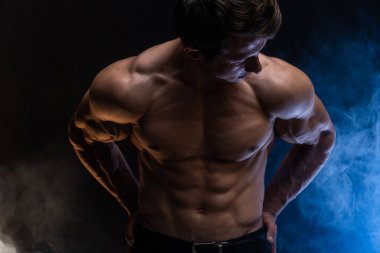 Siyah arka planda renkli dumanla izole edilmiş kasları gösteren kaslı bir adam. Sağlıklı yaşam tarzı kavramı 