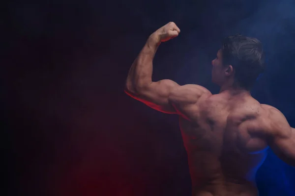 Bărbatul musculos arată mușchii izolați pe fundalul negru cu fum colorat. Conceptul de stil de viață sănătos — Fotografie, imagine de stoc