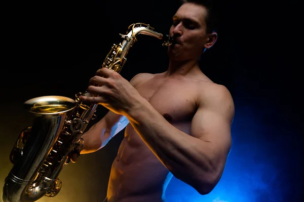 Homem muscular com tronco nu tocando no saxofone com fundo colorido fumado — Fotografia de Stock