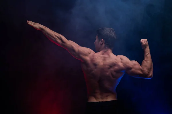 Muscular man showing muscles isolated on the black background with colored smoke. Concept of healthy lifestyle — Stock Photo, Image