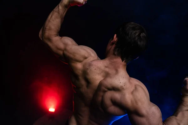 Uomo muscolare che mostra i muscoli isolati sullo sfondo nero con fumo colorato. Concetto di stile di vita sano — Foto Stock