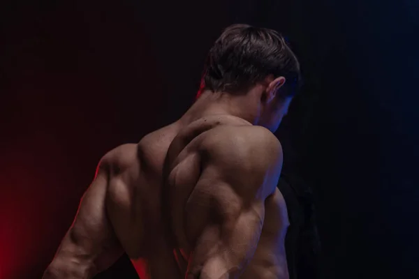 Gespierde man toont spieren geïsoleerd op de zwarte achtergrond met gekleurde rook. Concept van een gezonde levensstijl — Stockfoto