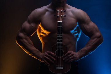 Ukulele ve füme renkli arka planı olan çıplak gövdeli kaslı bir adam. 