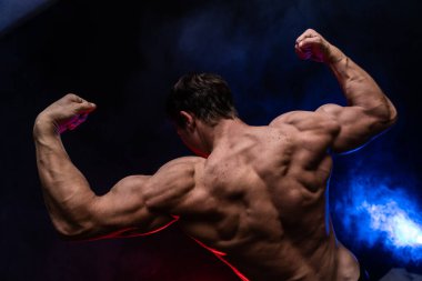 Siyah arka planda renkli dumanla izole edilmiş kasları gösteren kaslı bir adam. Sağlıklı yaşam tarzı kavramı 