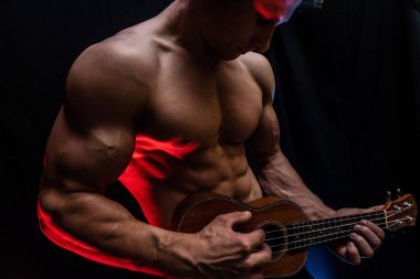 Ukulele ve füme renkli arka planı olan çıplak gövdeli kaslı bir adam. 