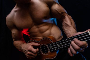 Ukulele ve füme renkli arka planı olan çıplak gövdeli kaslı bir adam. 