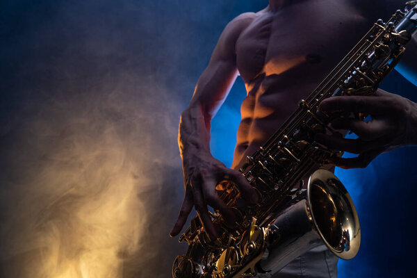 Мускулистый мужчина с голым туловищем, играющий на саксофоне с копченым красочным фоном
 
