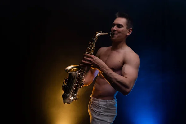 Homem muscular com tronco nu tocando no saxofone com fundo colorido fumado — Fotografia de Stock