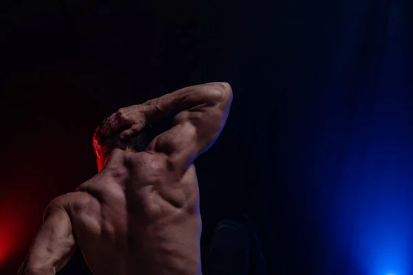 Gespierde man toont spieren geïsoleerd op de zwarte achtergrond met gekleurde rook. Concept van een gezonde levensstijl — Stockfoto