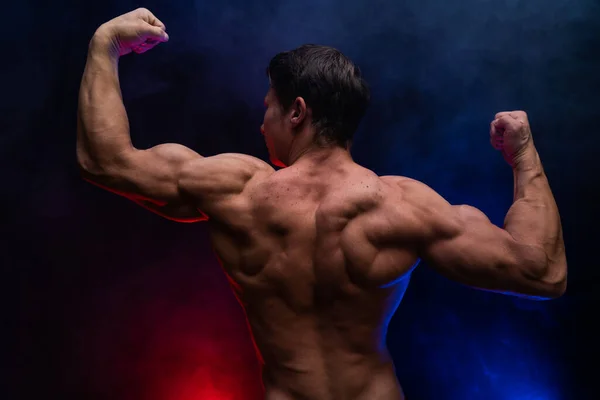 Hombre musculoso mostrando músculos aislados en el fondo negro con humo de color. Concepto de estilo de vida saludable — Foto de Stock