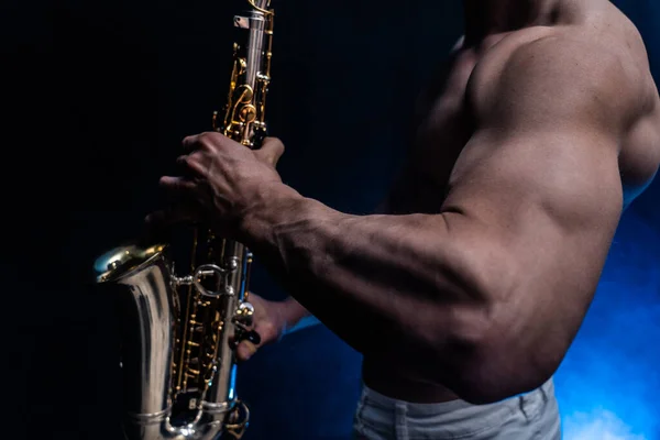 Uomo muscoloso con busto nudo che suona su sassofono con sfondo colorato affumicato — Foto Stock