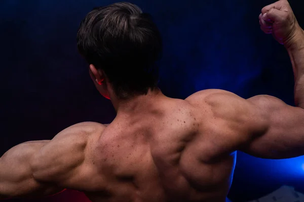 Hombre musculoso mostrando músculos aislados en el fondo negro con humo de color. Concepto de estilo de vida saludable —  Fotos de Stock