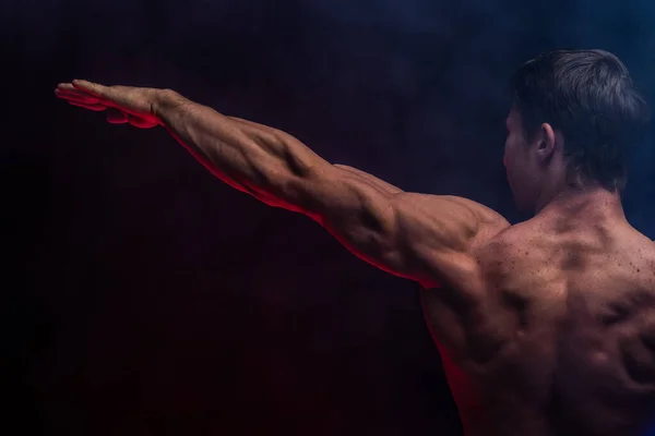 Gespierde man toont spieren geïsoleerd op de zwarte achtergrond met gekleurde rook. Concept van een gezonde levensstijl — Stockfoto