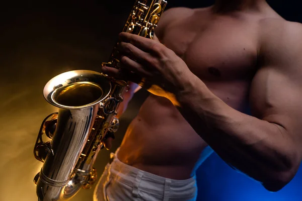 Muscular man with naked torso playing on saxophone with smoked colorful background — Stock Photo, Image