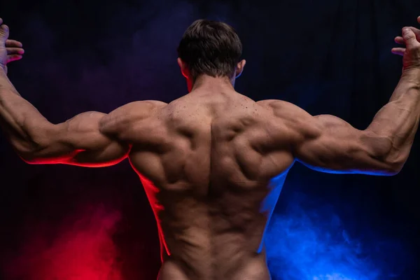 Muscular man showing muscles isolated on the black background with colored smoke. Concept of healthy lifestyle — Stock Photo, Image