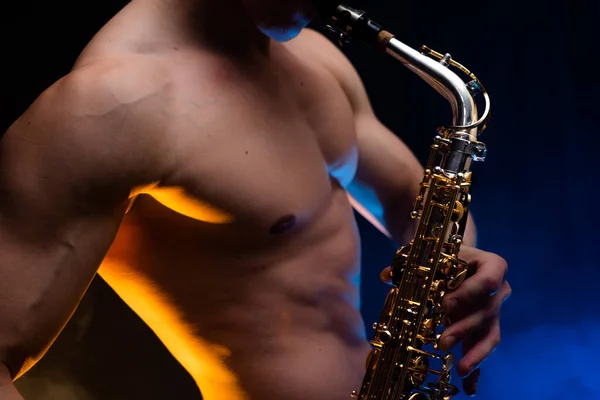 Muscular man with naked torso playing on saxophone with smoked colorful background — Stock Photo, Image