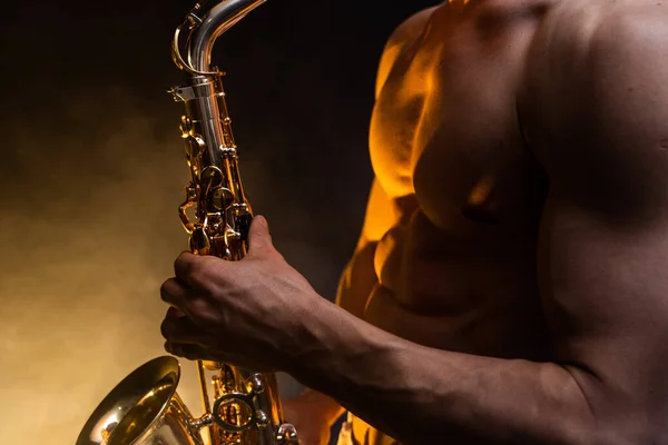 Muscular man with naked torso playing on saxophone with smoked colorful background — Stock Photo, Image