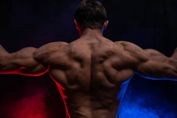 Hombre musculoso mostrando músculos aislados en el fondo negro con humo de color. Concepto de estilo de vida saludable —  Fotos de Stock