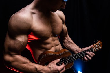 Ukulele ve füme renkli arka planı olan çıplak gövdeli kaslı bir adam. 