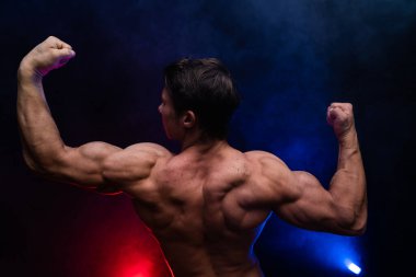 Siyah arka planda renkli dumanla izole edilmiş kasları gösteren kaslı bir adam. Sağlıklı yaşam tarzı kavramı 