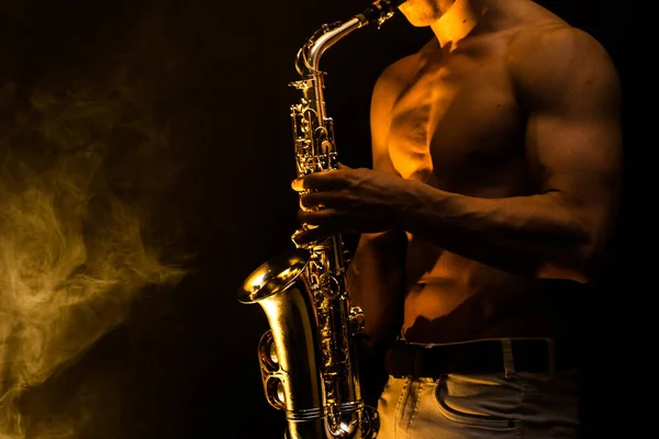 Muskulös man med naken bål spelar på saxofon med rökt färgglad bakgrund — Stockfoto